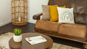 A brown leather sofa with multiple cushions, a round wooden coffee table with a white vase and magazine, and a wicker floor lamp. - Villa with private pool in Vilamoura (Vilamoura)