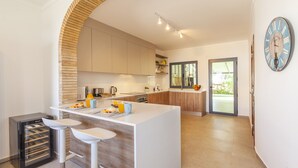 Una cocina moderna con una isla central, taburetes de bar, un refrigerador y un reloj en la pared.