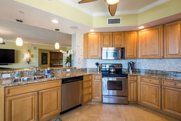 A modern kitchen with granite countertops, stainless steel appliances, wooden cabinets, and pendant lighting. - 5th Floor Luxury Condo with Gulf Views and Steps from the Beach (Clearwater)