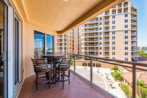 A balcony with a table and chairs, overlooking a courtyard with potted plants and a building complex. - 5th Floor Luxury Condo with Gulf Views and Steps from the Beach (Clearwater)