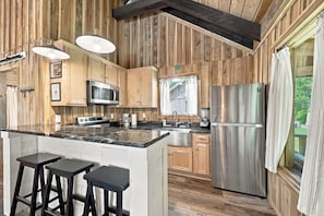 Une cuisine avec des murs en bois, un réfrigérateur en acier inoxydable, un four à micro-ondes, une cuisinière et des tabourets de bar.