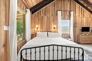 Ein Schlafzimmer mit einem Bett, zwei Wandlampen, einem Fernseher und einem Fenster mit Vorhängen.