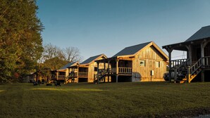 A row of wooden cabins with a grassy yard and a large tree to the left. - Waterfall Basecamp Cabin, Near Rock Island & Hiking (Smithville)