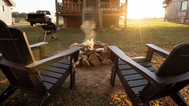 A rustic cabin with a fire pit in the center, surrounded by Adirondack chairs. - Waterfall Basecamp Cabin, Near Rock Island & Hiking (Smithville)