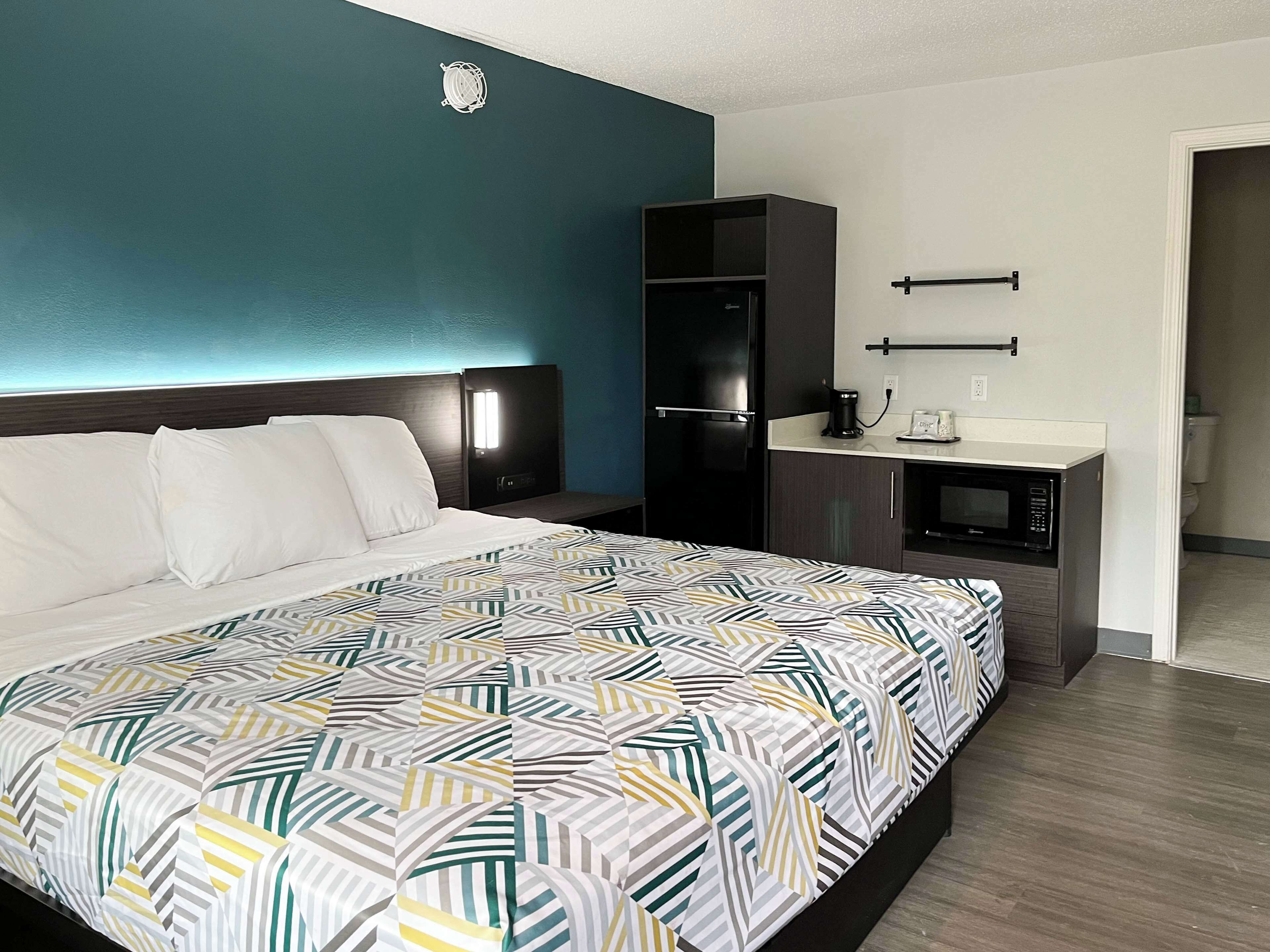 A hotel room with a bed, a small kitchenette, and a bathroom.