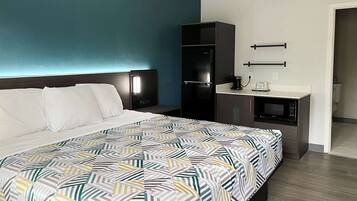 A hotel room with a bed, a small kitchenette, and a bathroom.