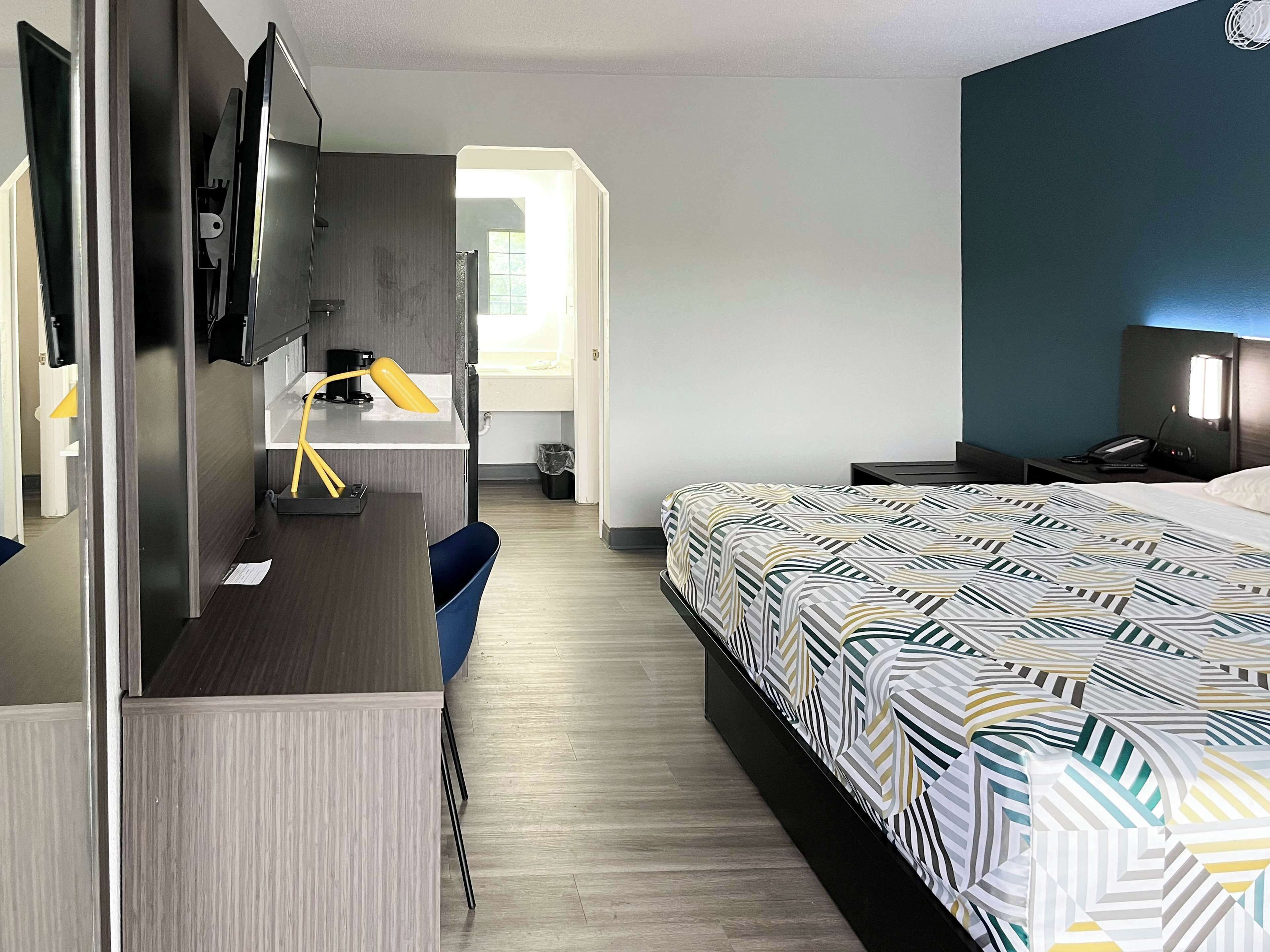 Hotellihuone, jossa on sänky, työpöytä tuolilla, televisio ja pieni pöytä.