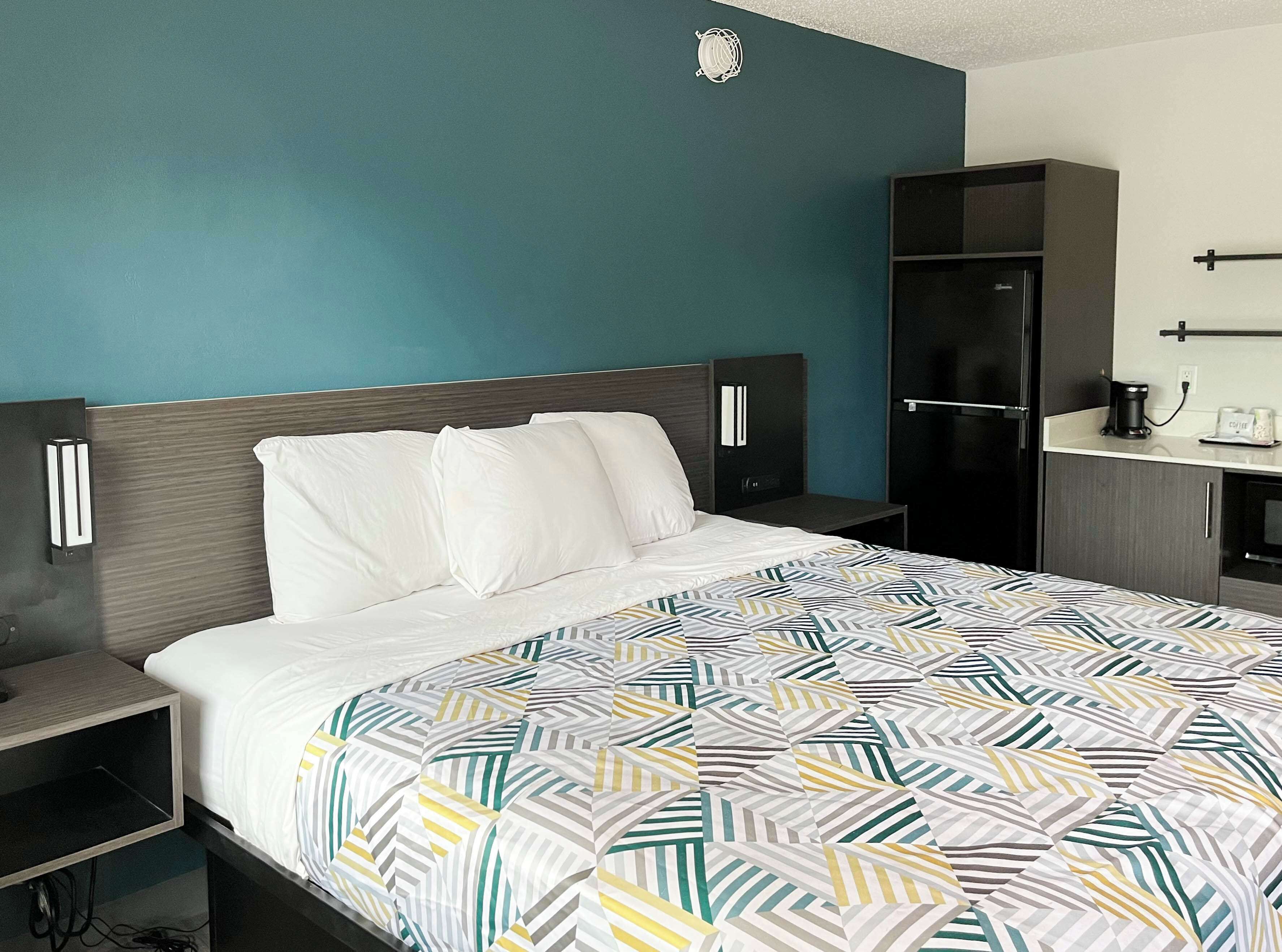 A hotel room with a bed, a nightstand, a wardrobe, and a small kitchenette area.