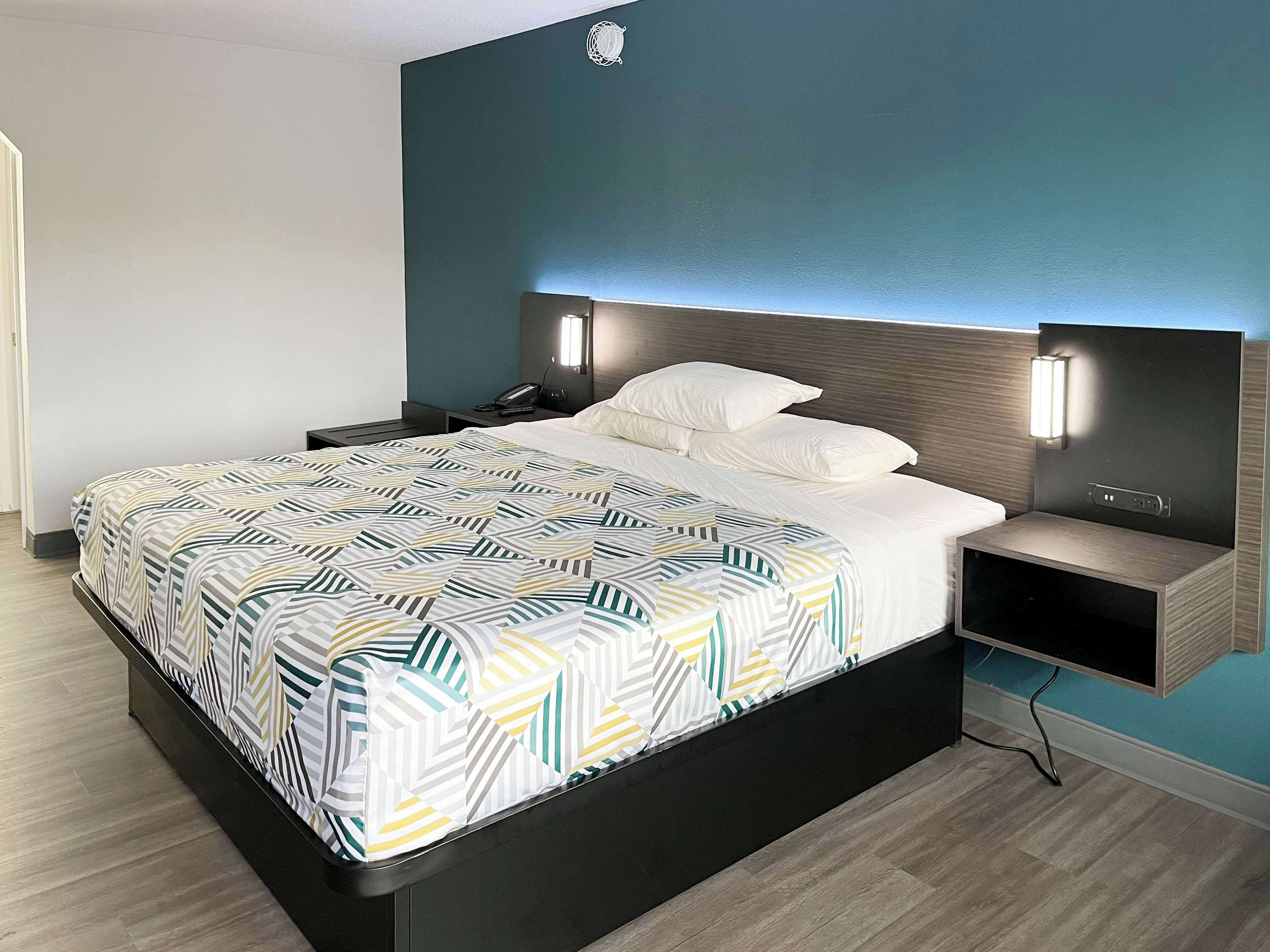 A modern hotel room with a large bed, bedside tables, and a wall-mounted light fixture.