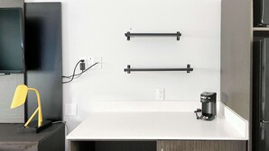 A modern office space with a desk, chair, and a coffee machine. There are two black metal bars mounted on the wall, and a TV is visible on the left. - Studio 6 Suites - Lafayette, IN (Lafayette)