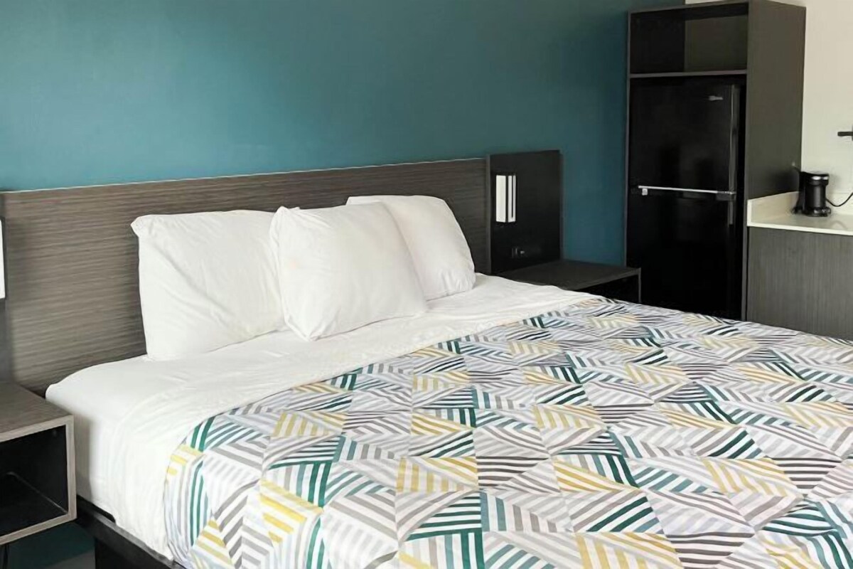 A hotel room with a bed, a nightstand, a wardrobe, and a desk with a chair.