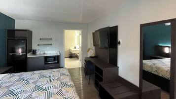 A hotel room with a bed, a desk, a TV, a mirror, and a kitchenette.