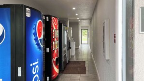 A hallway with vending machines, including Pepsi and Coca-Cola, and a door leading to a bright area. - Studio 6 Suites - Lafayette, IN (Lafayette)