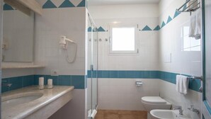 A bathroom with a shower, toilet, and sink, featuring blue and white tiles and a small window. - Superb Residenze del Golfo di Orosei No2197 (Orosei)