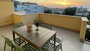A balcony with a table and chairs, a potted plant, and a view of buildings and a sunset. - MAISON LARA - Luxury home in the center of Sorrento (Sorrento)