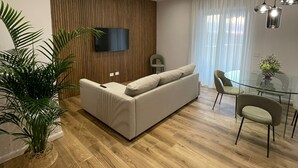 A modern living room with a sofa, a TV mounted on the wall, a dining table with chairs, and a large potted plant. - MAISON LARA - Luxury home in the center of Sorrento (Sorrento)
