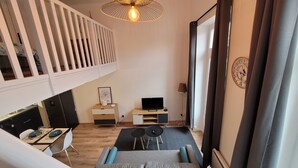Ein modernes Wohnzimmer mit Schlafgalerie, einem Esstisch und einem Fernseher auf einem Holzboden.