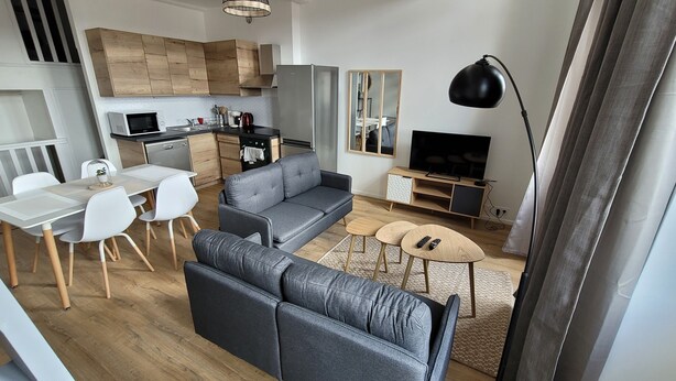 Un apartamento moderno con comedor, sofá gris, televisor y cocina.