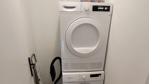 Un cuarto de lavandería con dos lavadoras apiladas y una aspiradora.