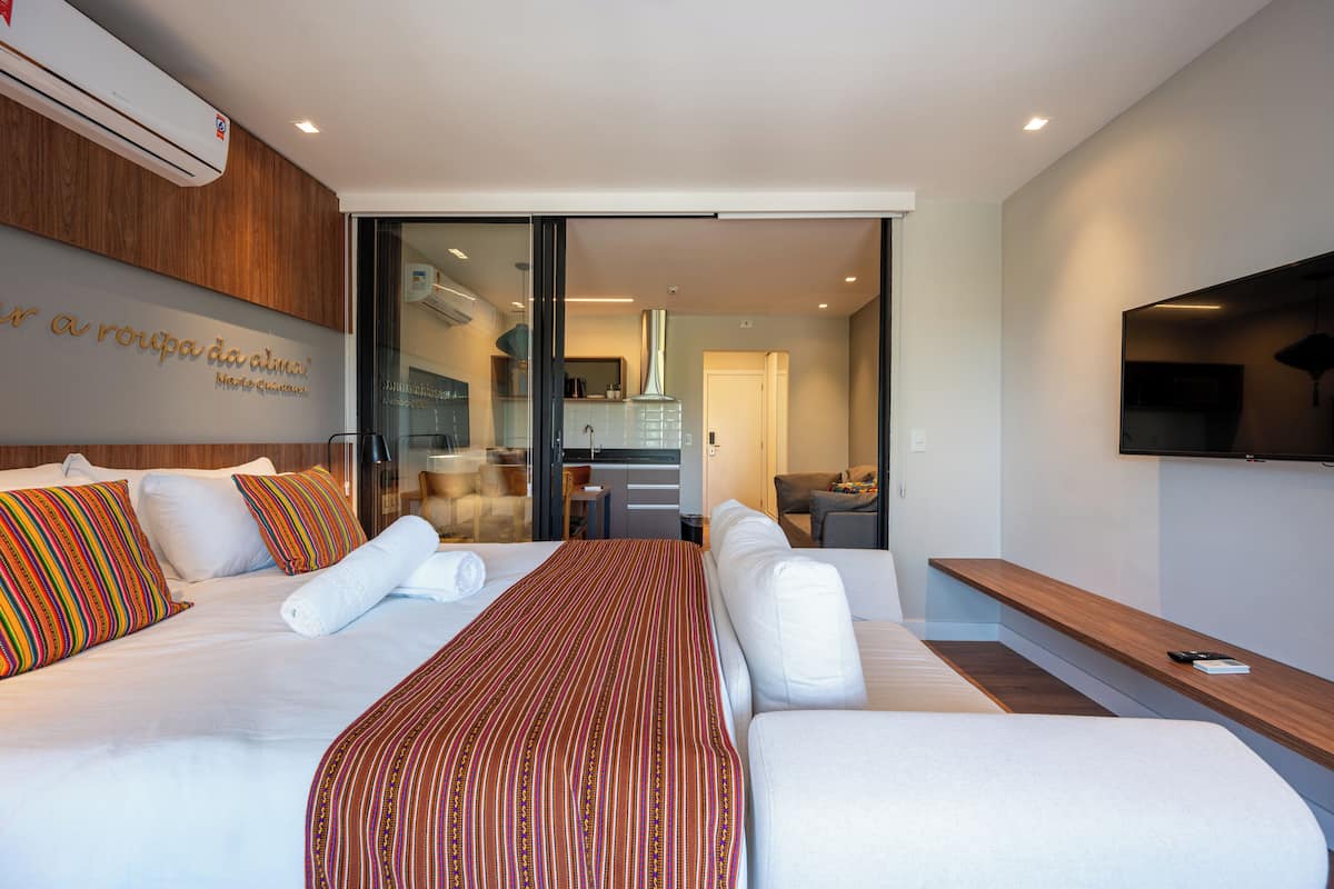Una habitación de hotel moderna con una cama grande, un televisor de pantalla plana y una puerta corrediza de vidrio que da a una zona de cocina.