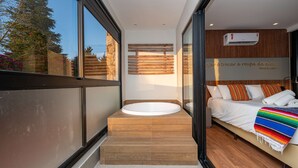 Ein modernes Badezimmer mit einer freistehenden Badewanne, einer Holzbank und einem Bett mit bunter Decke.