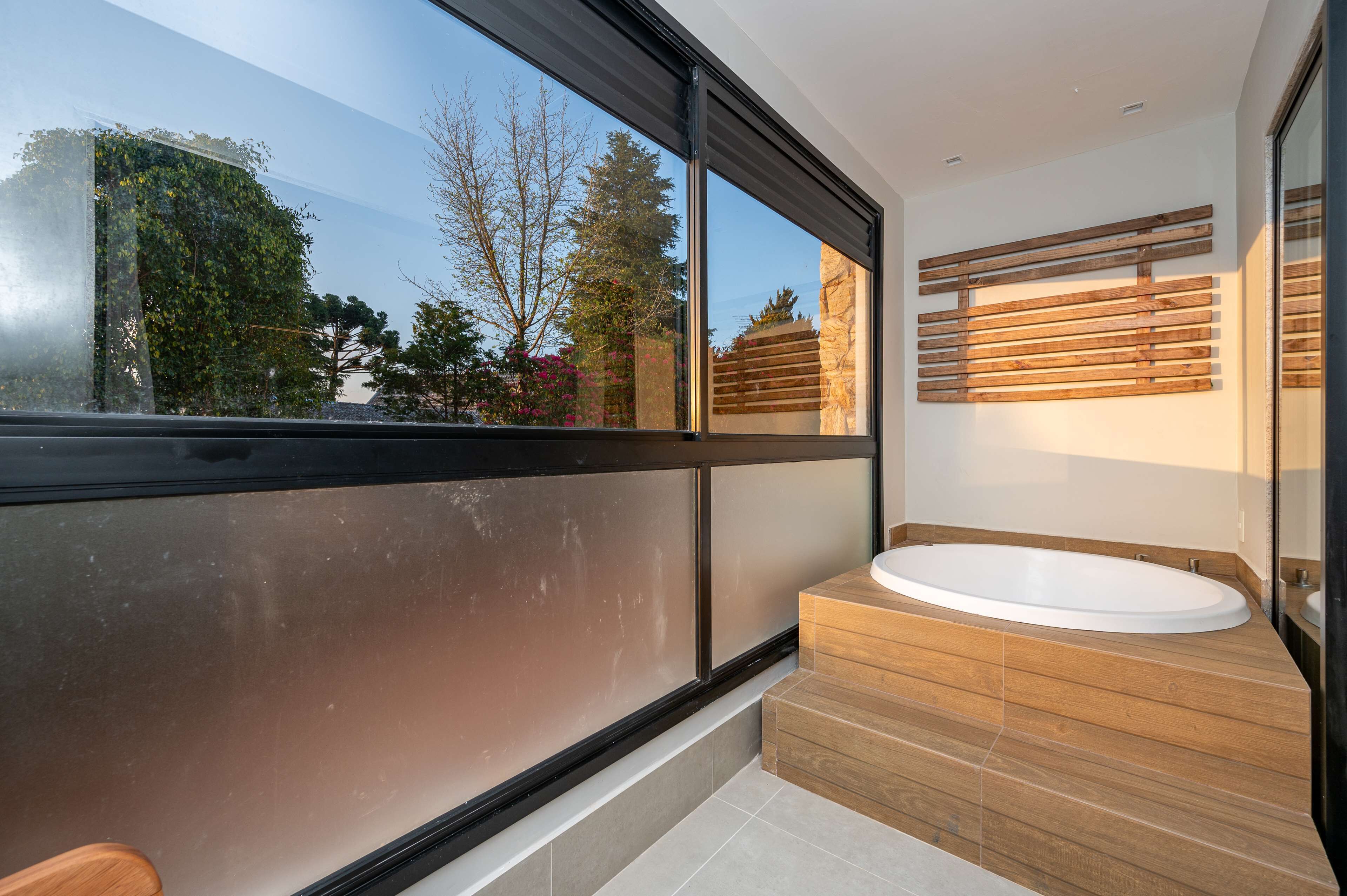 Un baño moderno con un ventanal grande, una bañera independiente y un tocador de madera.