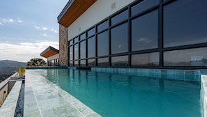 Ein moderner Poolbereich mit freiem Blick auf die umliegende Landschaft, einer Steinmauer und einem großzügigen Gebäude mit Panoramafenstern.