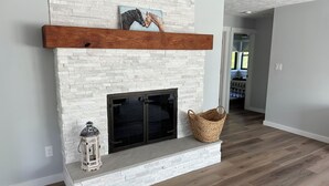 A modern living room with a white brick fireplace, a wooden mantel, and a woven basket. - 🐎 2 Miles to Flintfields, Fenced Yard pet friendly, FREE RENTAL Golf Cart (Williamsburg)