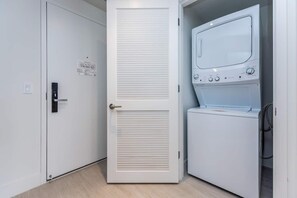 A laundry room with a white washing machine and dryer, a door with a handle, and a small sign on the wall. - This impressive 2-bedroom corner apartment combines elegance, comfort, and breathtaking views (Hollywood)