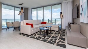 A modern hotel room with a large window, a sofa, a coffee table, and a TV. - This impressive 2-bedroom corner apartment combines elegance, comfort, and breathtaking views (Hollywood)