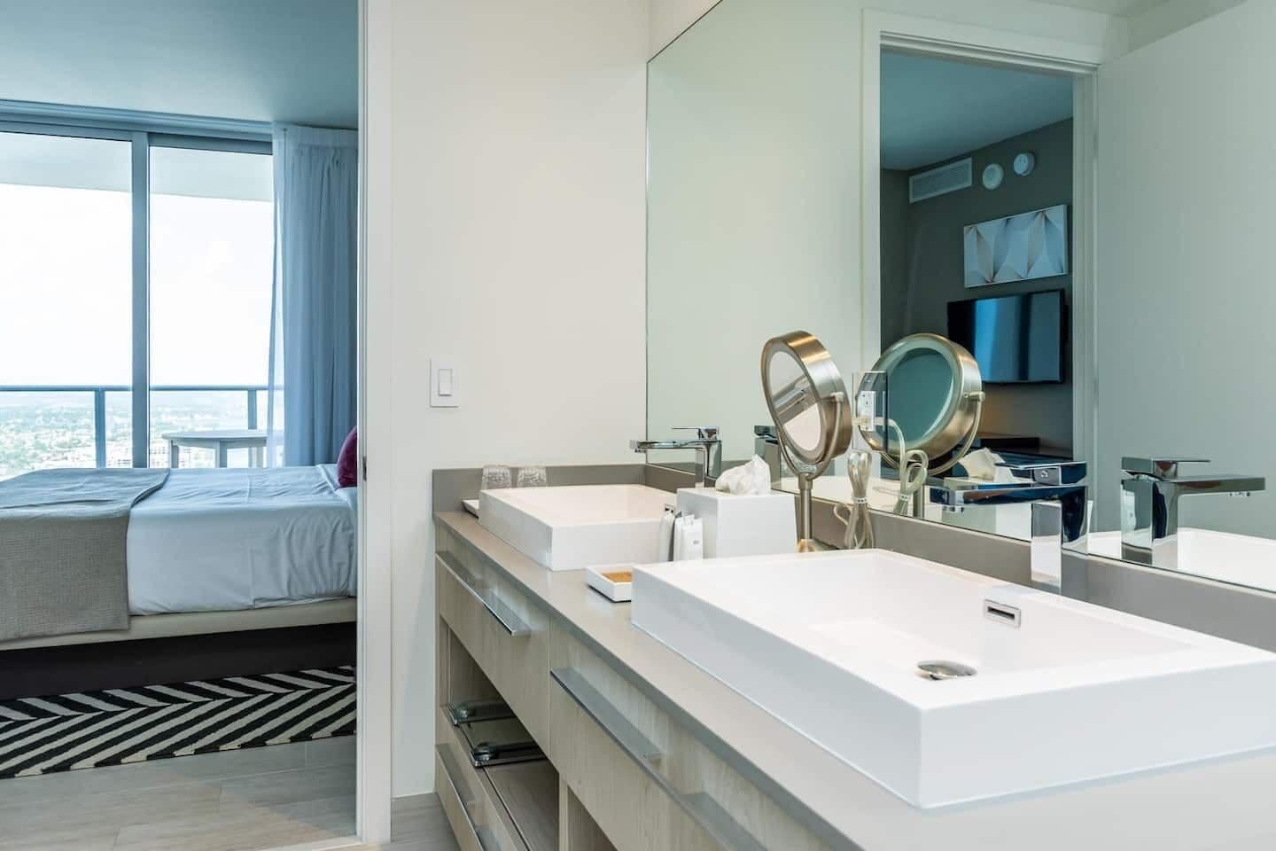 Une chambre d’hôtel moderne avec un grand lit, un double lavabo et un grand miroir.
