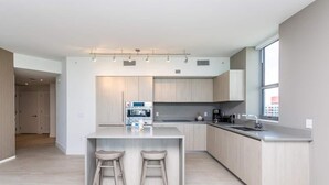 A modern kitchen with a central island, two bar stools, a built-in oven, and a large window. - This impressive 2-bedroom corner apartment combines elegance, comfort, and breathtaking views (Hollywood)