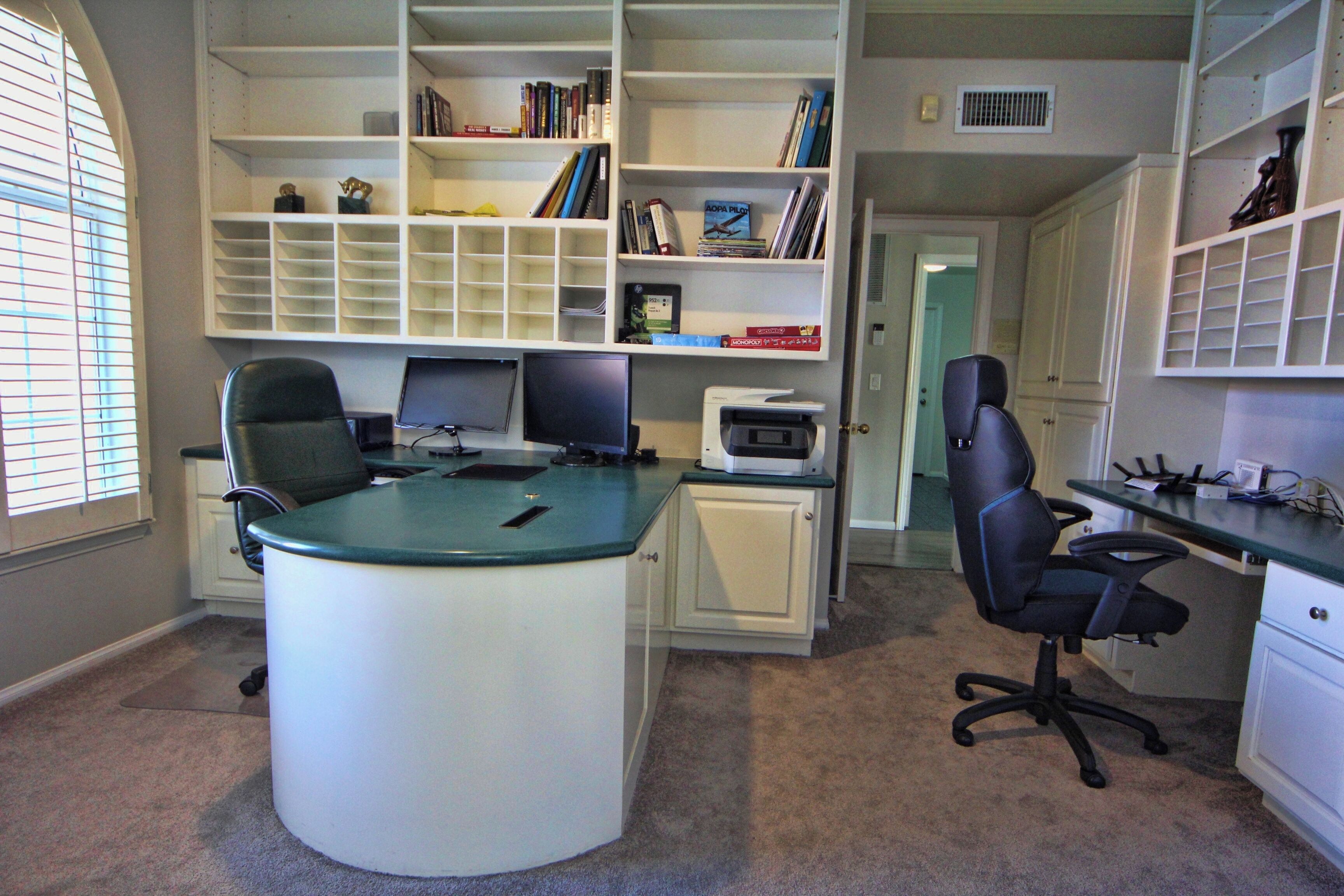A home office with a desk, two chairs, a computer, and a bookshelf filled with books.