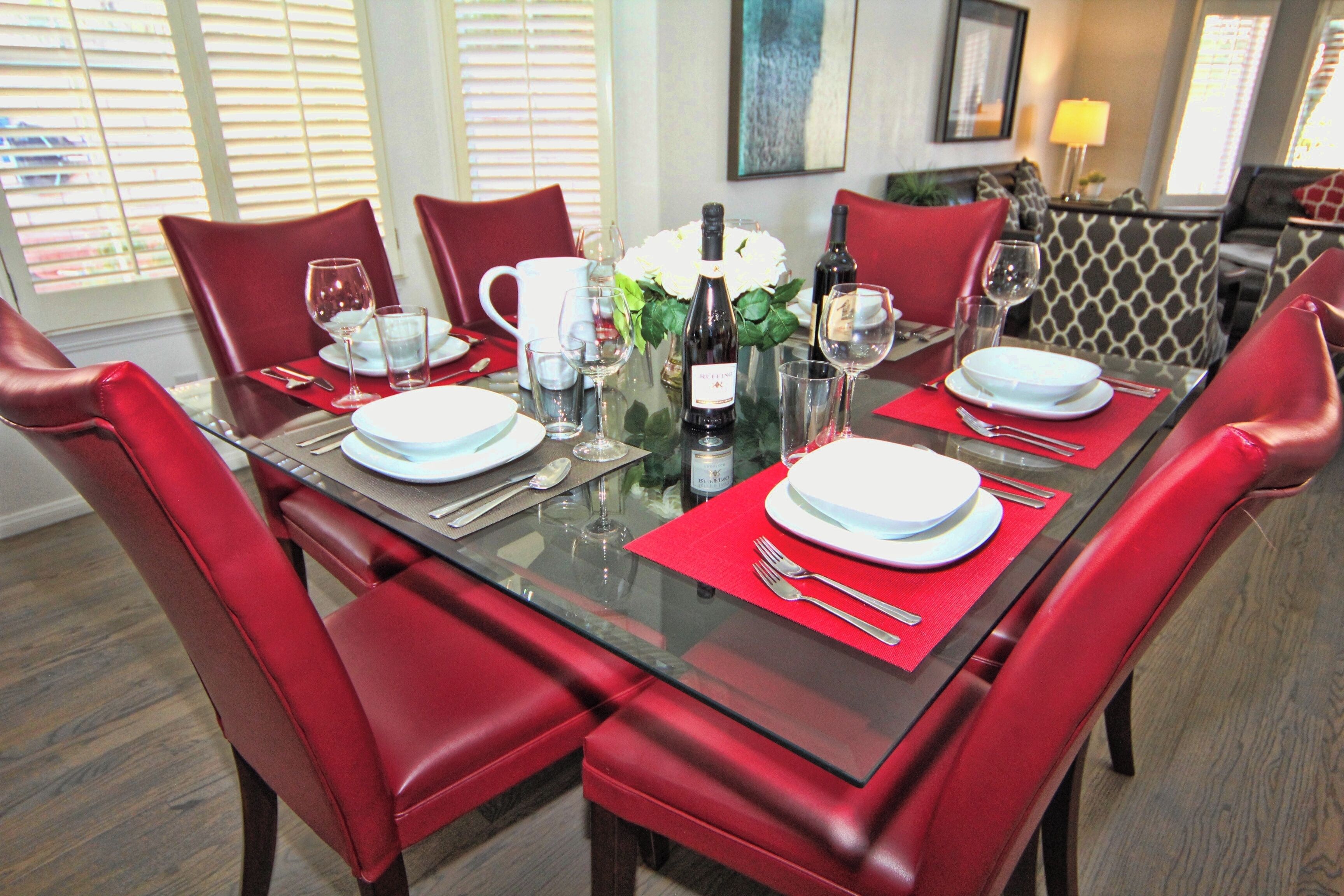 A dining table set with red chairs, white plates, and wine glasses.