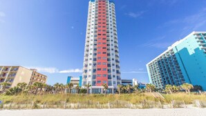 A tall, multi-story hotel with a distinctive red and white facade, located near a beach with palm trees and a sandy foreground. - NEW! Palace Resort TRUE Oceanfront STUDIO Condo (Myrtle Beach)