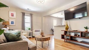 A modern living room with a sofa, coffee table, TV, and wooden shelves. - Charming Park Circle Bungalow with Screened Porch (North Charleston)