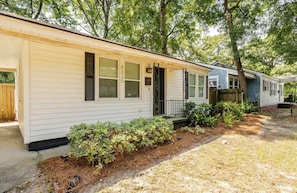 A single-story mobile home with a front porch, a mailbox, and a small garden area with shrubs.