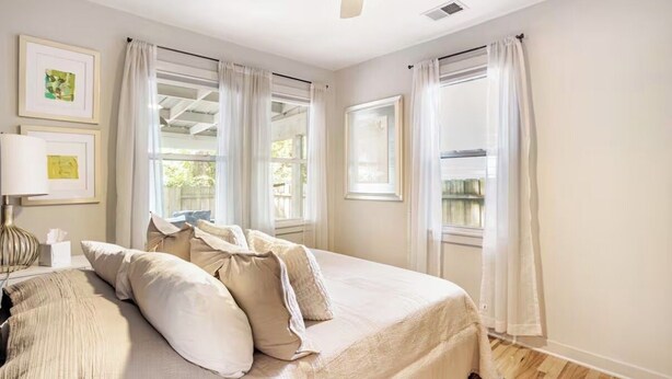 A bedroom with a bed, a ceiling fan, and large windows with curtains. - Charming Park Circle Bungalow with Screened Porch (North Charleston)