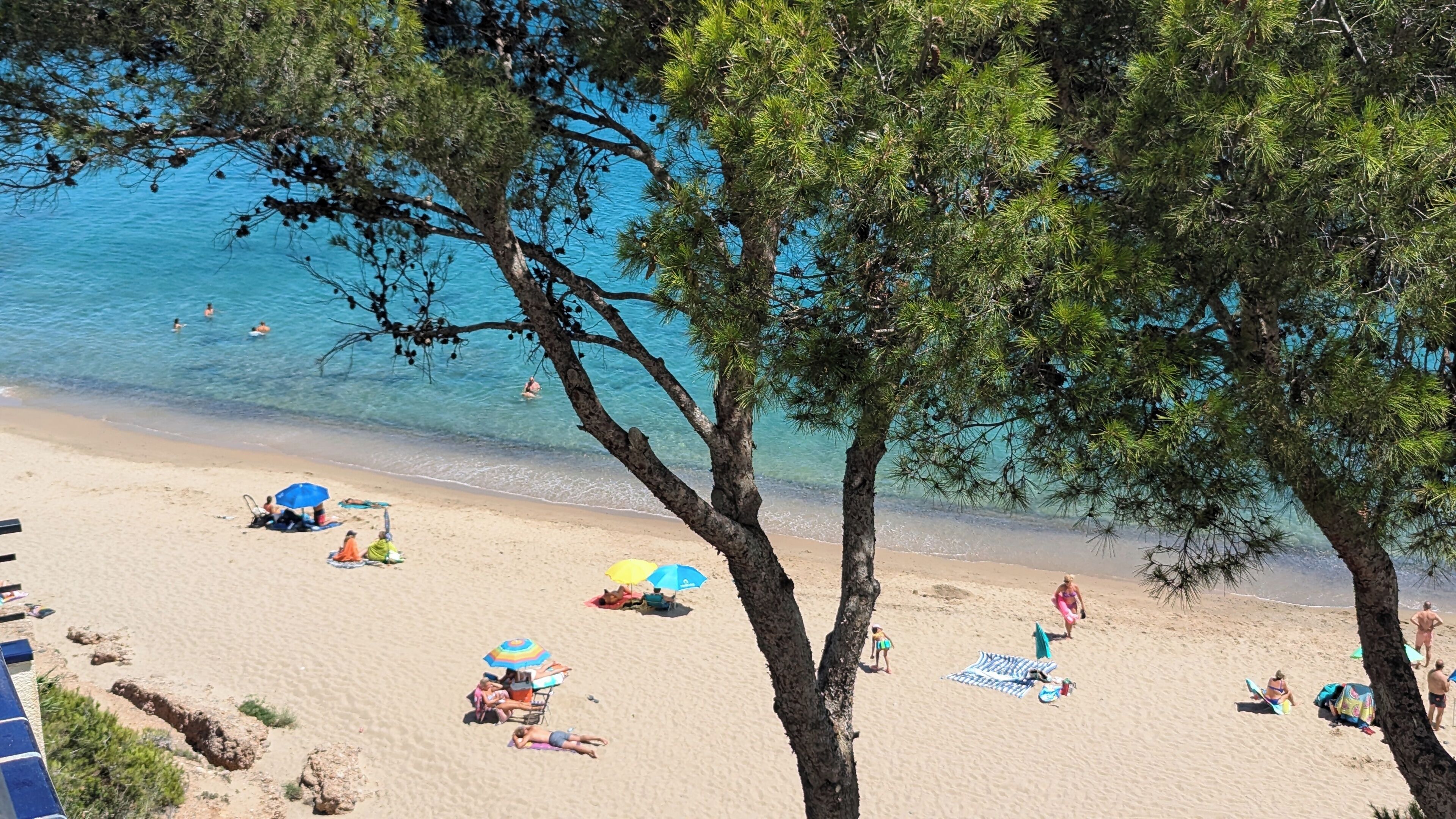 Ein Strand mit badenden Personen, Sonnenschirmen und einem klaren, blauen Meer.
