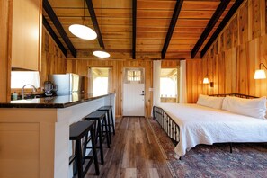 A wooden interior with a kitchen, bar stools, a bed, and a patterned rug.