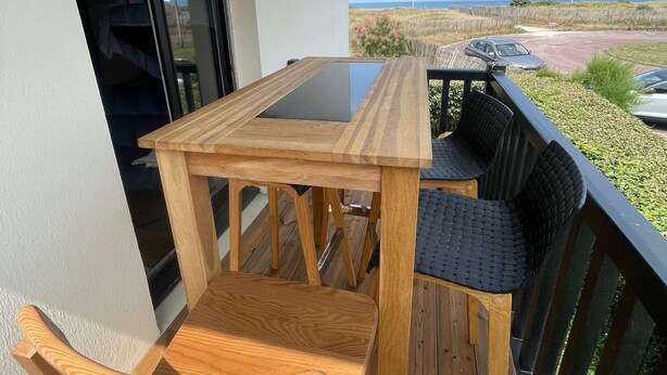 A wooden deck with a table and chairs, a sliding glass door, and a view of the beach and ocean. - Joli Studio Avec Balcon en Bord de mer (Cabourg)