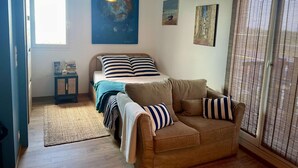 A bedroom with a bed, a sofa, a small cabinet, and artwork on the walls. - Joli Studio Avec Balcon en Bord de mer (Cabourg)