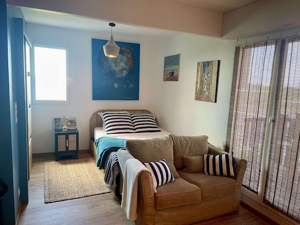A bedroom with a bed, a sofa, a small cabinet, and artwork on the walls.