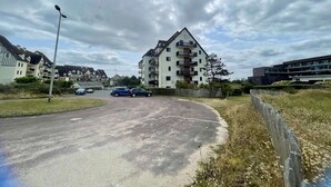 A residential area with a multi-story apartment building, a curved road, and parked cars. - Joli Studio Avec Balcon en Bord de mer (Cabourg)
