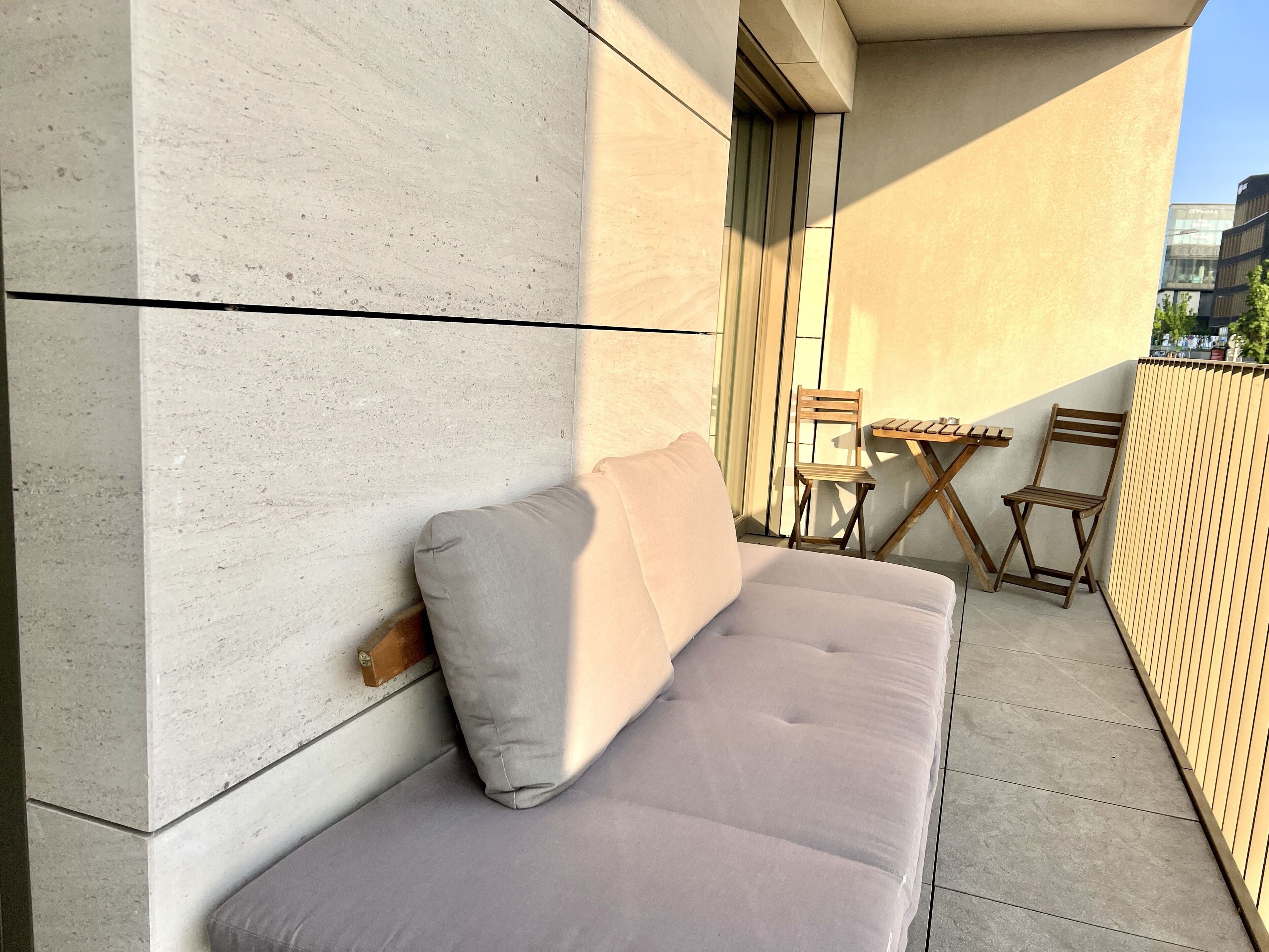 A modern outdoor seating area with a cushioned bench and a wooden table, adjacent to a building with a concrete facade.