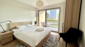 Un dormitorio moderno con una cama grande, una mesita de noche, un escritorio, una silla y vistas al exterior.