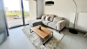 Una sala moderna con un sofá, una mesa de centro, una lámpara de pie y un ventanal corredizo que da a un balcón.