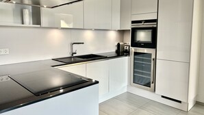 Una cocina moderna con armarios blancos, una encimera negra, una campana de acero inoxidable y un horno empotrado.