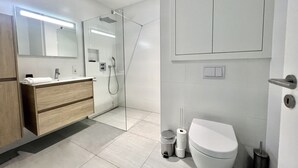 Un baño moderno con ducha de vidrio, inodoro blanco y tocador con espejo.