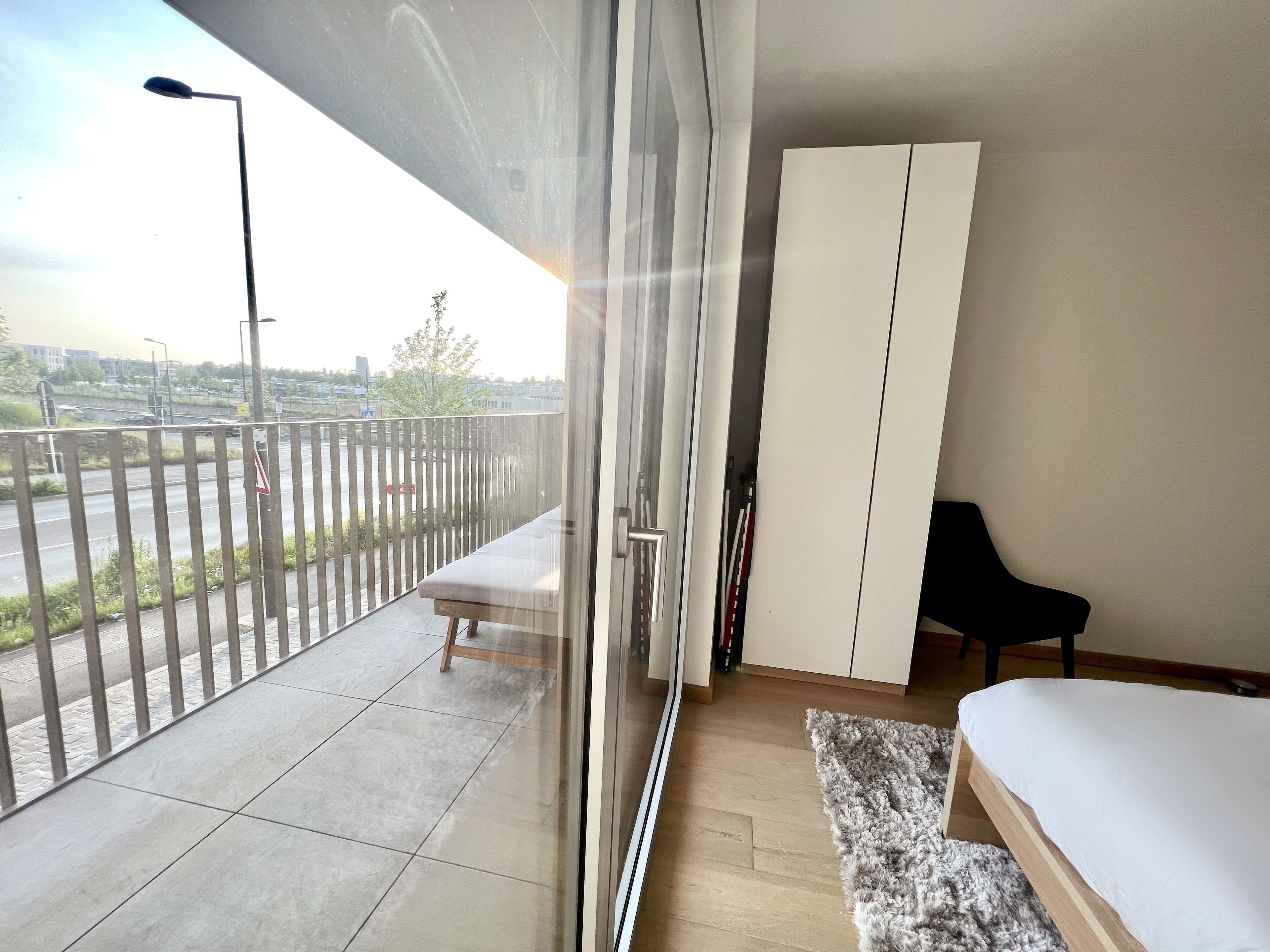 A balcony with a view of a road and buildings, a sofa, a bed, and a wardrobe.
